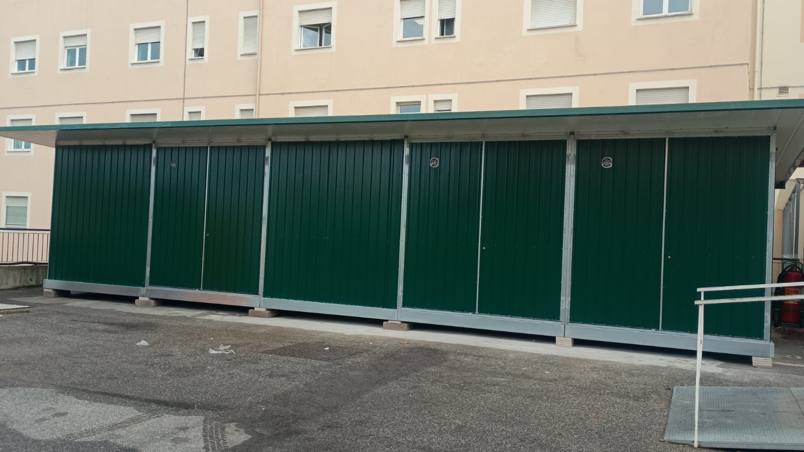 Armadietti di metallo verdi all'esterno di un edificio con finestre, sotto un tetto verde.