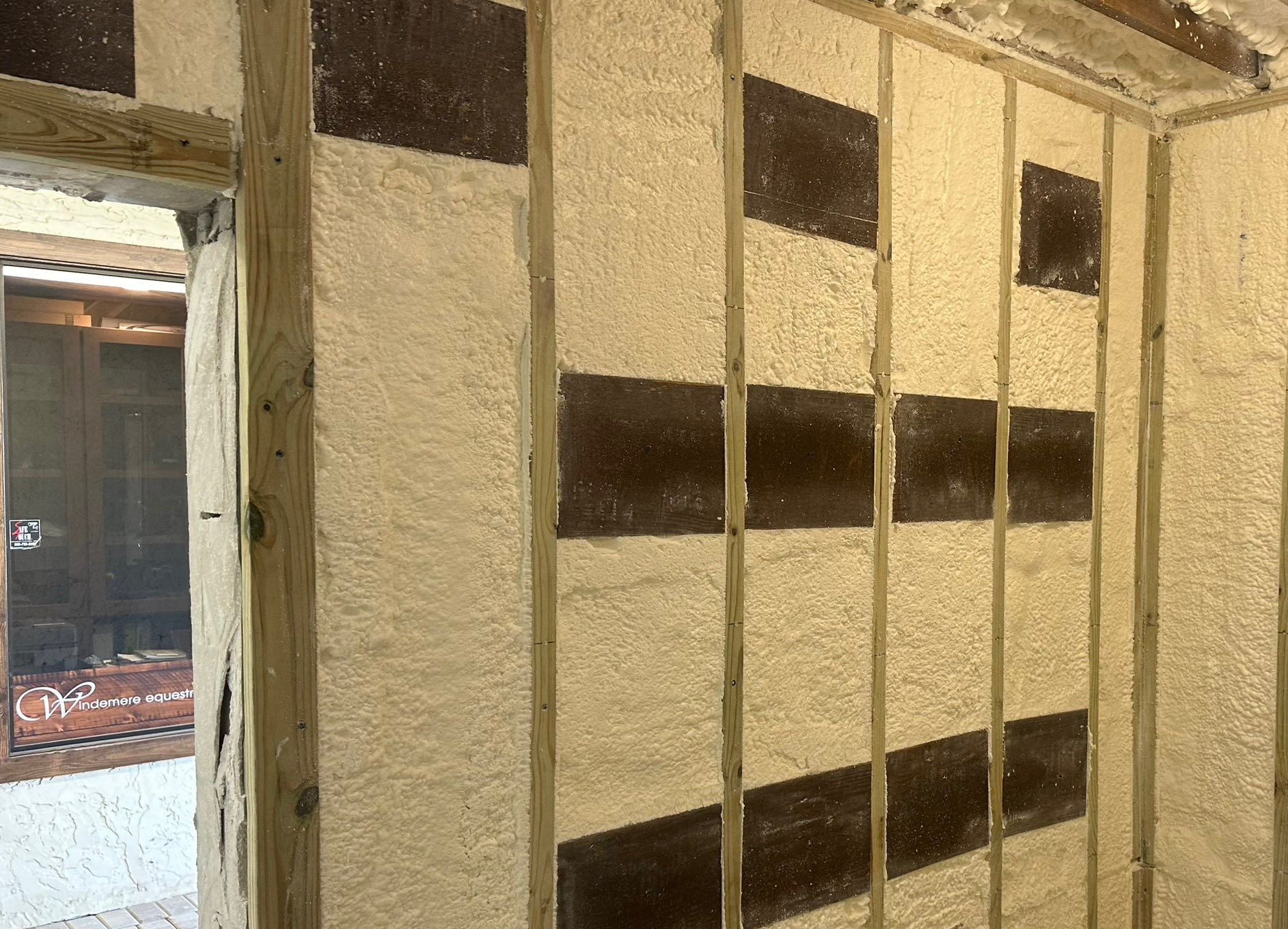 Person installing pink fiberglass insulation in a wooden wall frame.