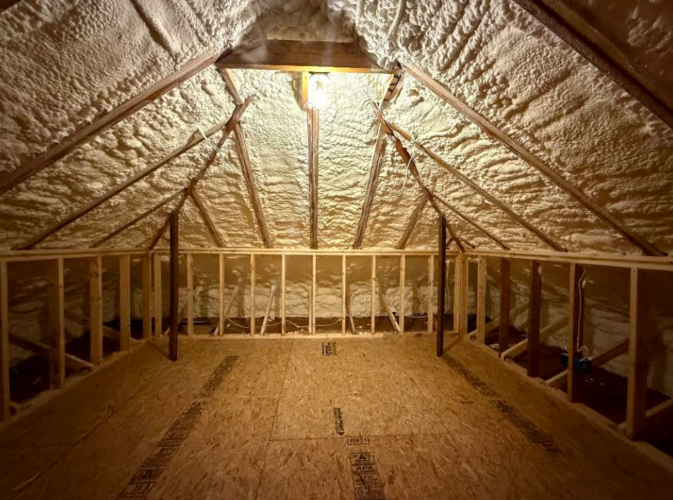 Person installing pink fiberglass insulation in a wooden wall frame.