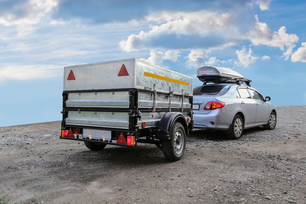 Silver car towing a utility trailer on a dirt road, under a cloudy sky. — All Auto & Mechanical in The Entrance North, NSW