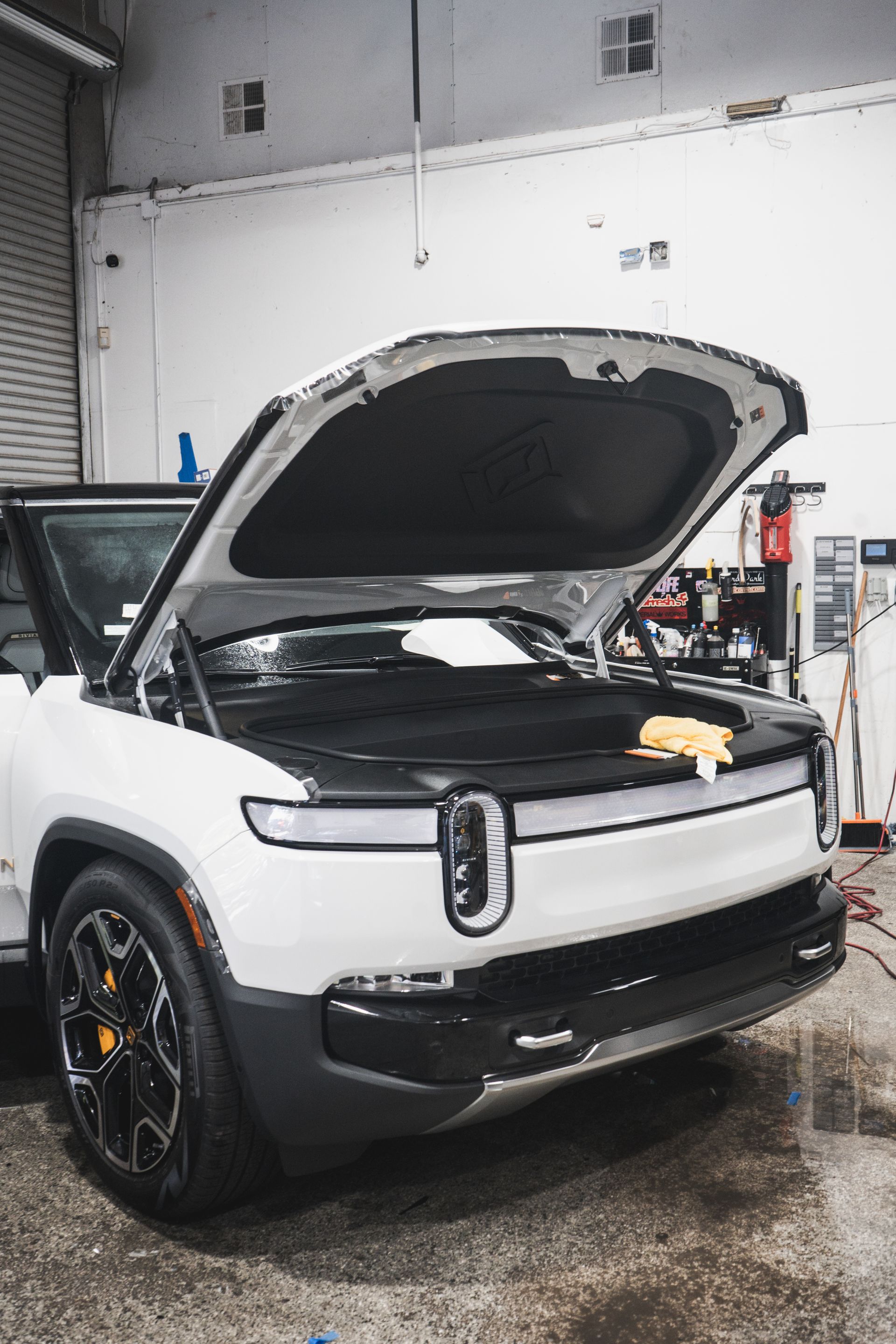 A white car with the hood open is parked in a garage.