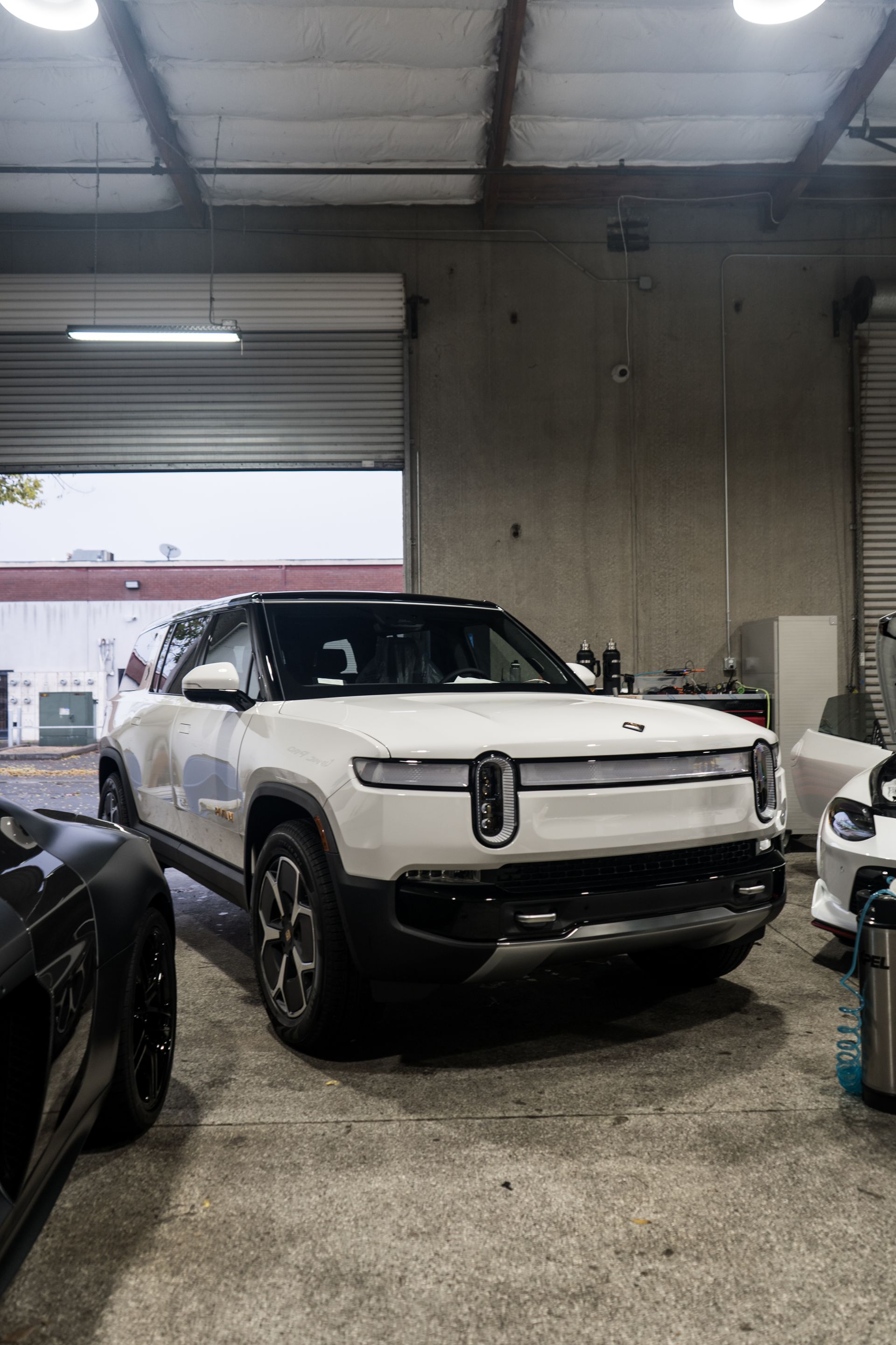 A white suv is parked in a garage next to a black car.