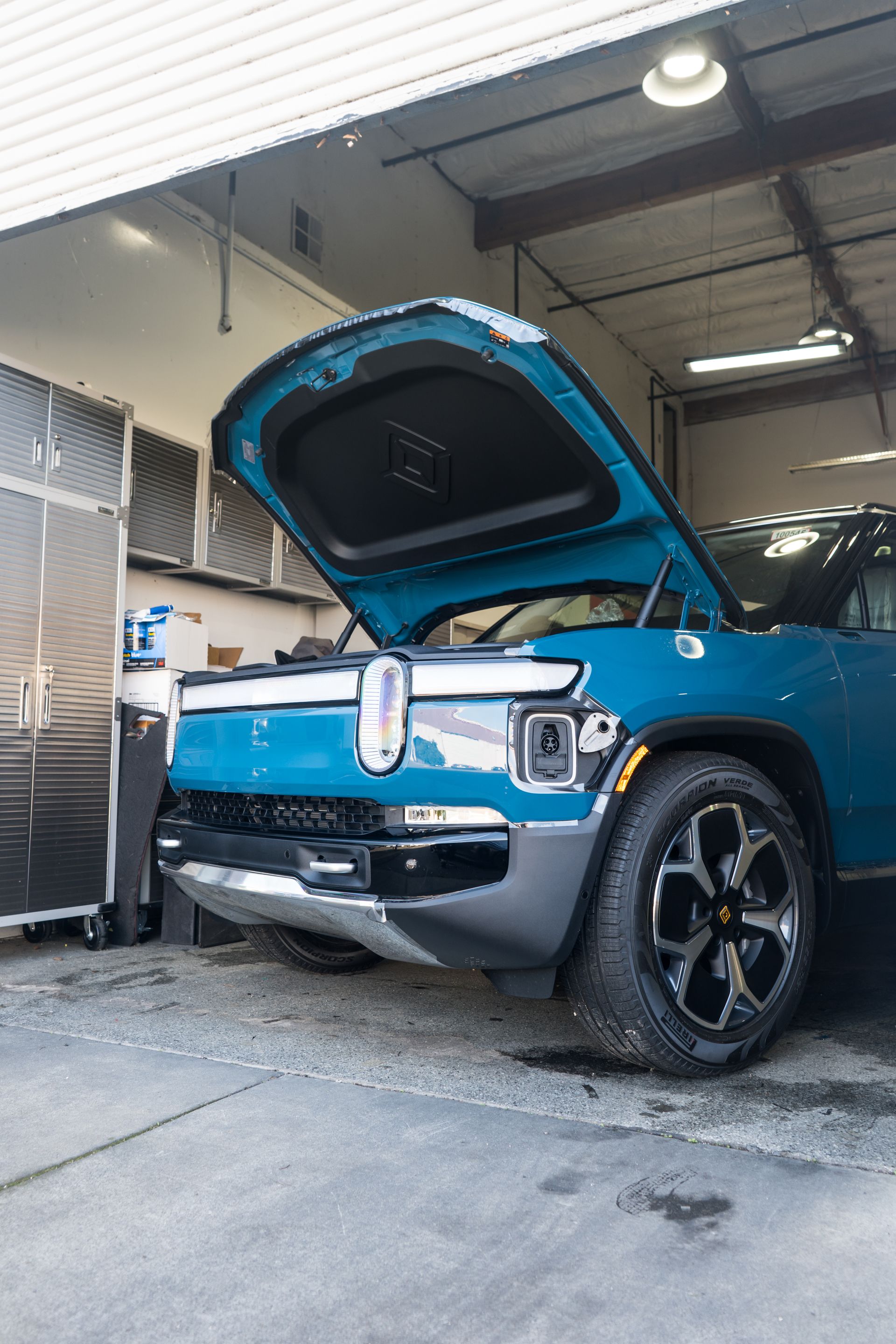 A blue car with the hood up is parked in a garage.