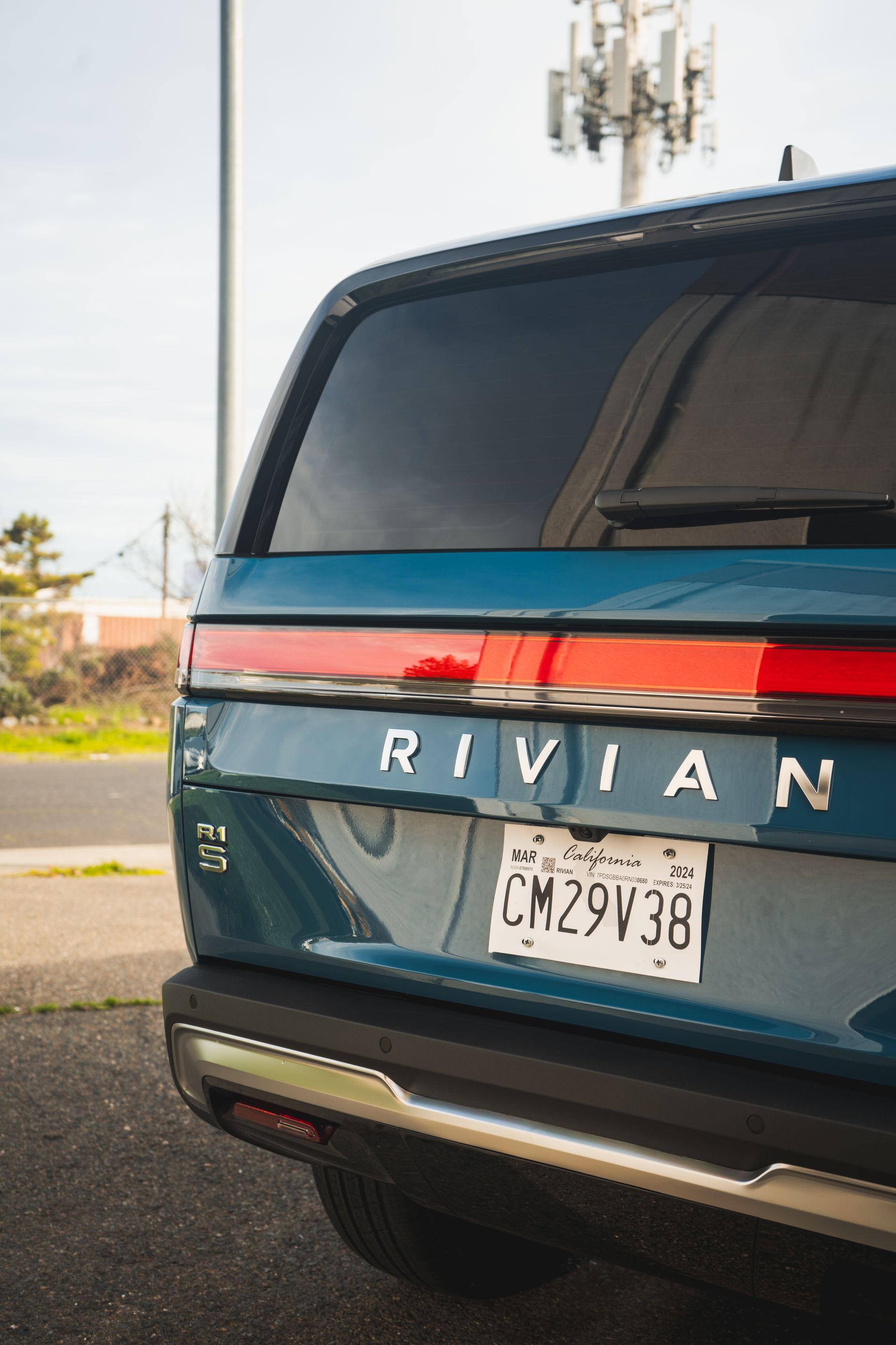 The back of a blue rivian suv is parked on the side of the road.