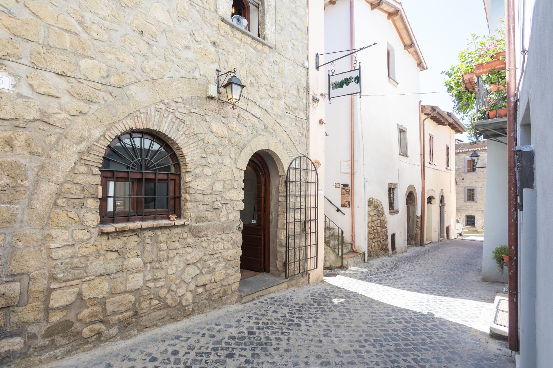 Stretta via acciottolata con edifici in pietra e bianchi in un antico e soleggiato borgo.