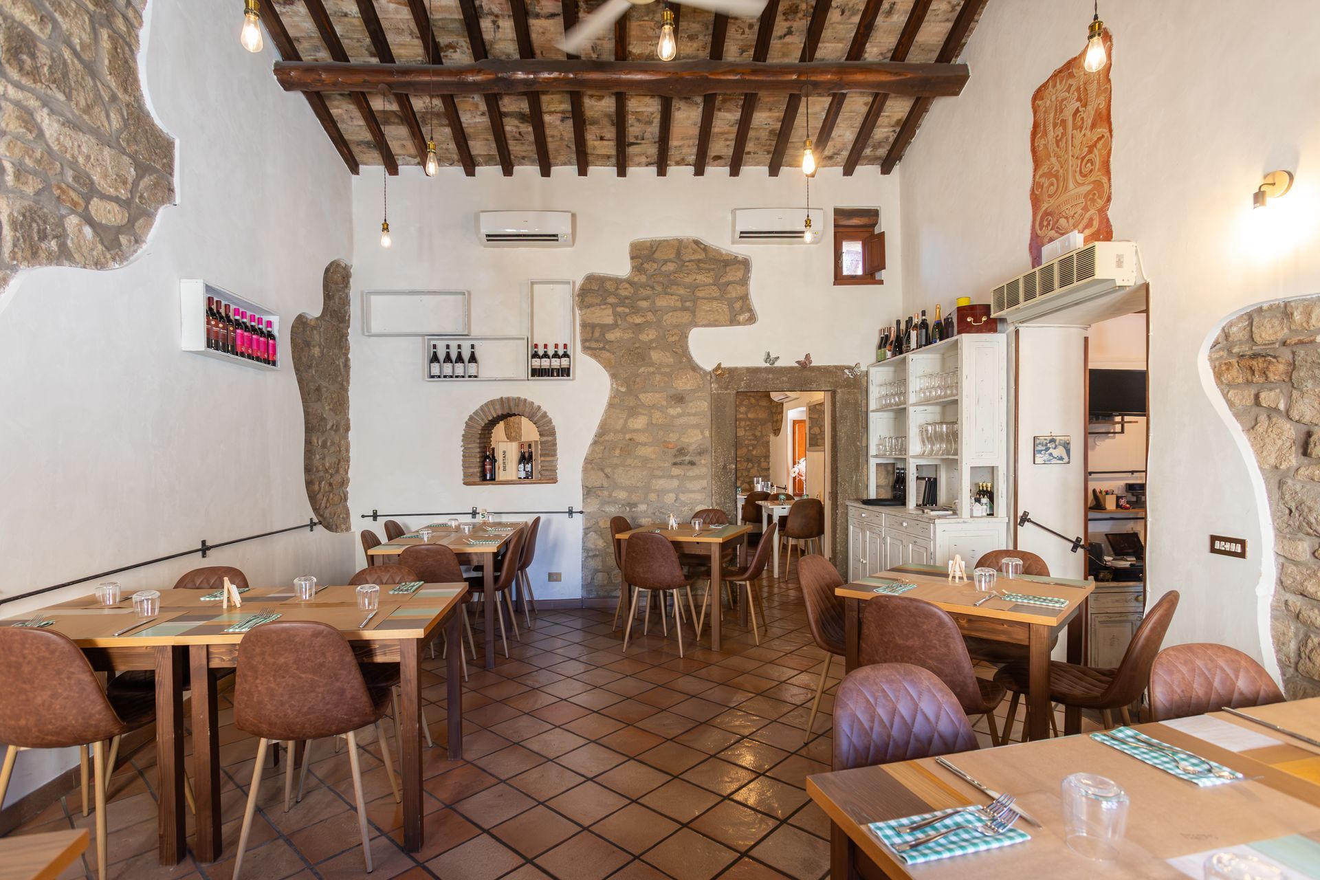 Accogliente interno rustico di un ristorante con tavoli in legno, pavimento in cotto e pareti e travi in pietra a vista.