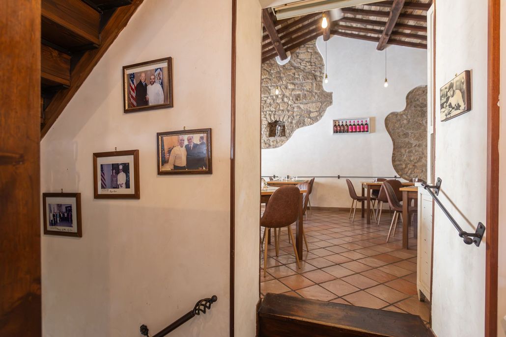 Corridoio con scale che si apre su una sala da pranzo rustica con foto incorniciate e pavimento piastrellato.