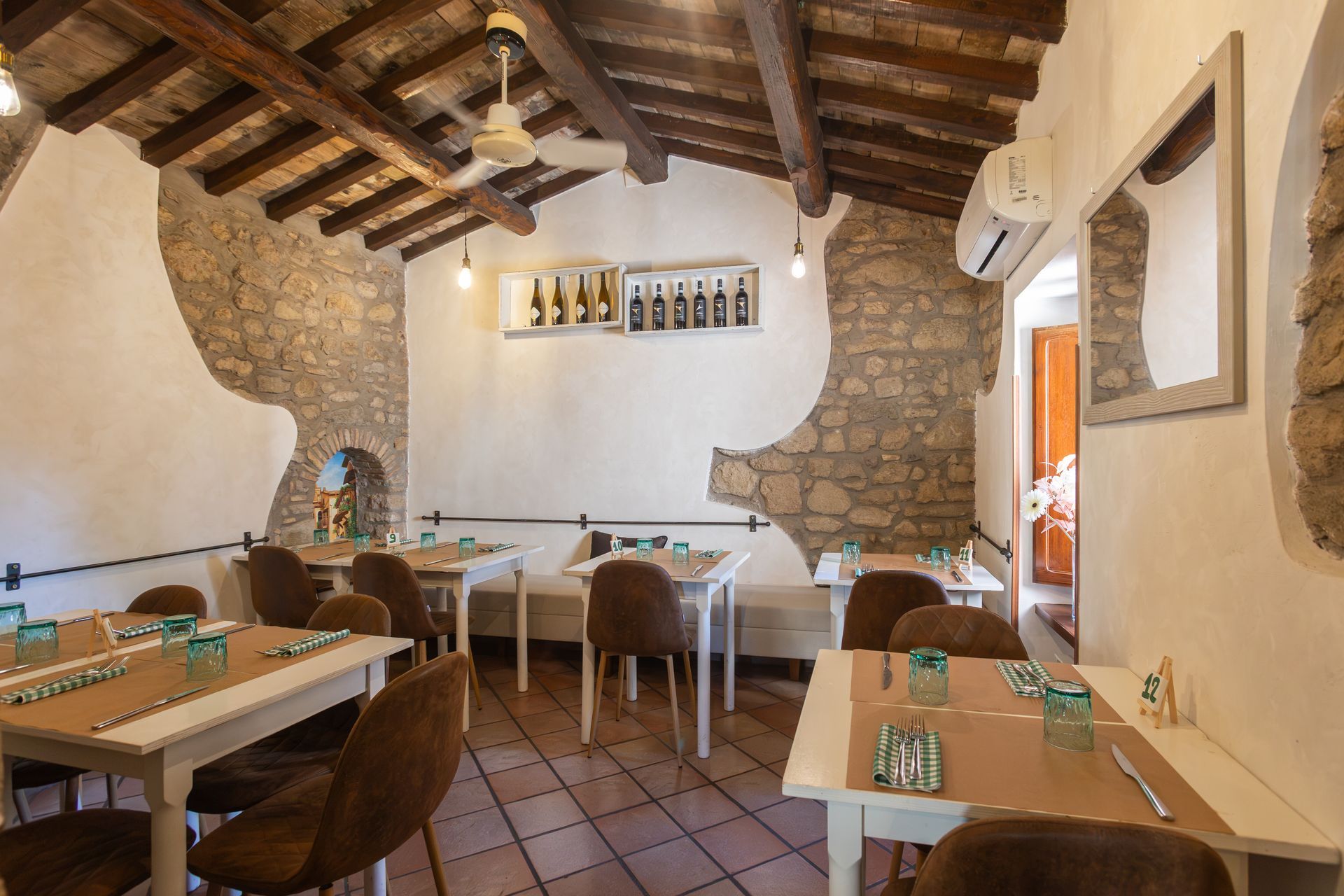 Interno rustico del ristorante con travi in legno, pareti in pietra e tavolini apparecchiati per la cena.