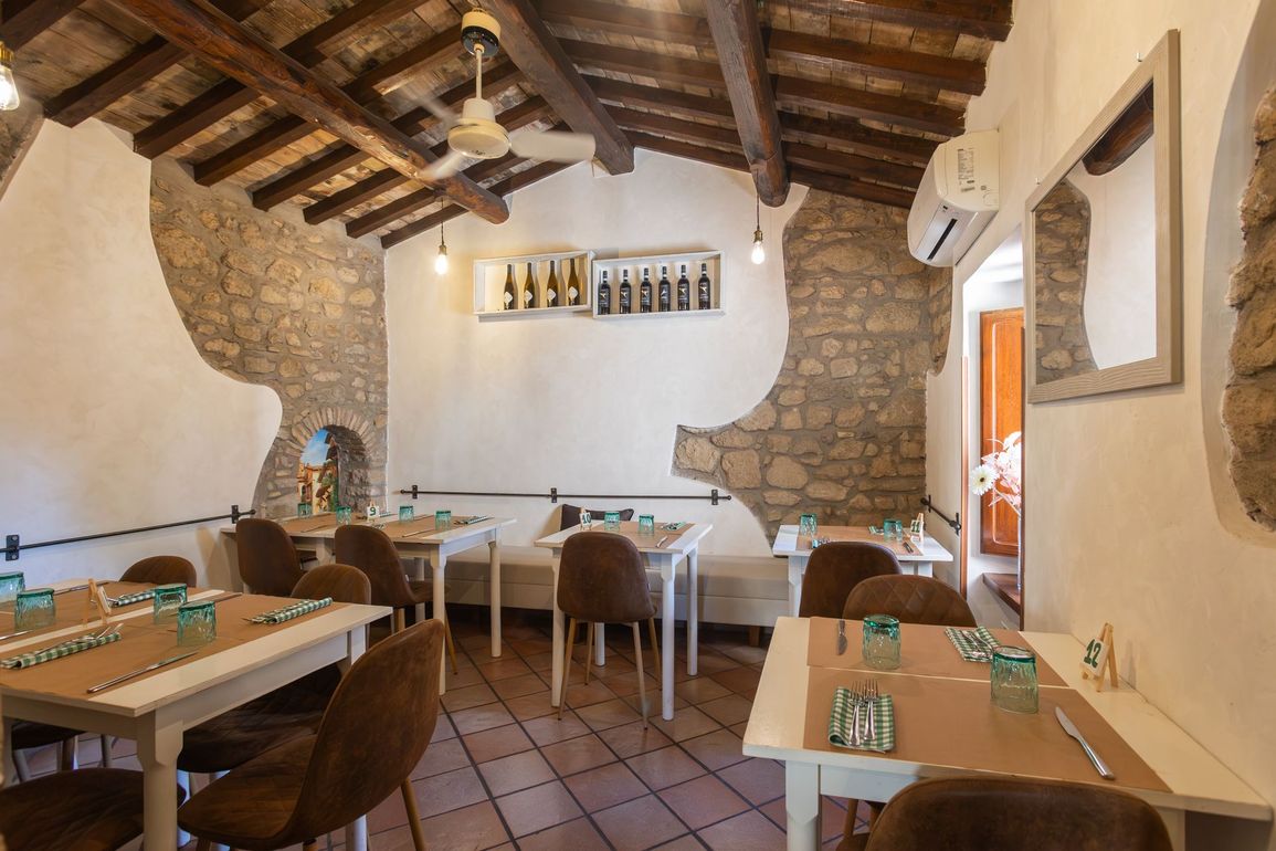 Interno rustico del ristorante con travi in ​​legno, pareti in pietra e tavolini apparecchiati per la cena.