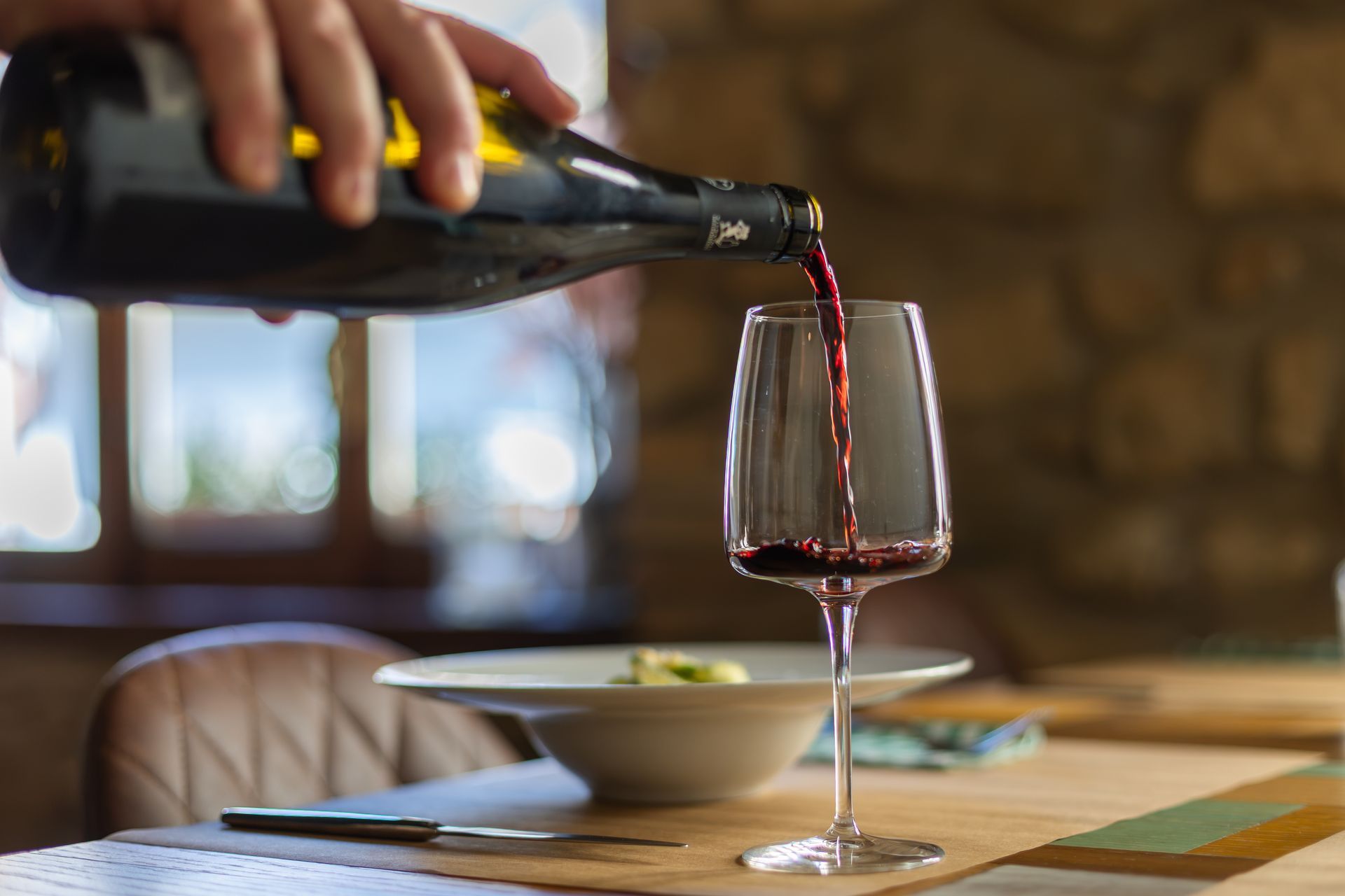In un accogliente ristorante, una mano versa del vino rosso in un calice a un tavolo.