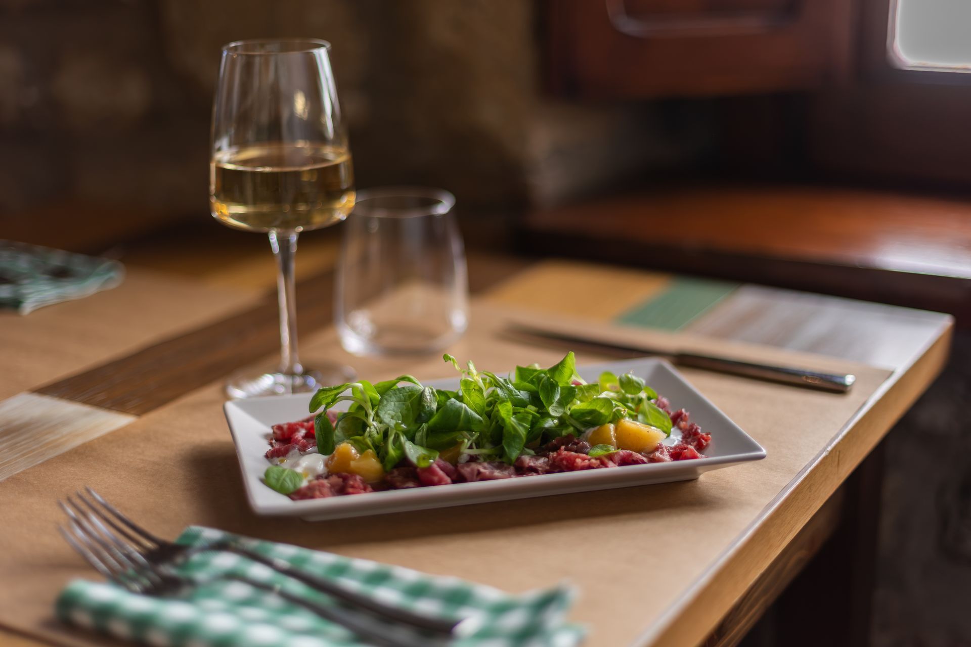 Un piatto da insalata e un bicchiere da vino bianco su un tavolo di legno nell'accogliente atmosfera di un ristorante.