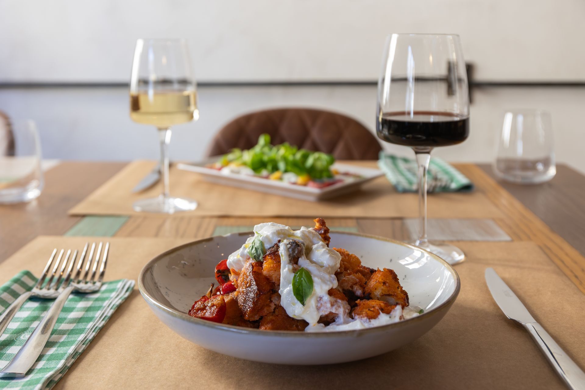 Tavolo da pranzo con pasta impiattata, bicchieri da vino, posate e un'ambientazione sfocata in stile ristorante.