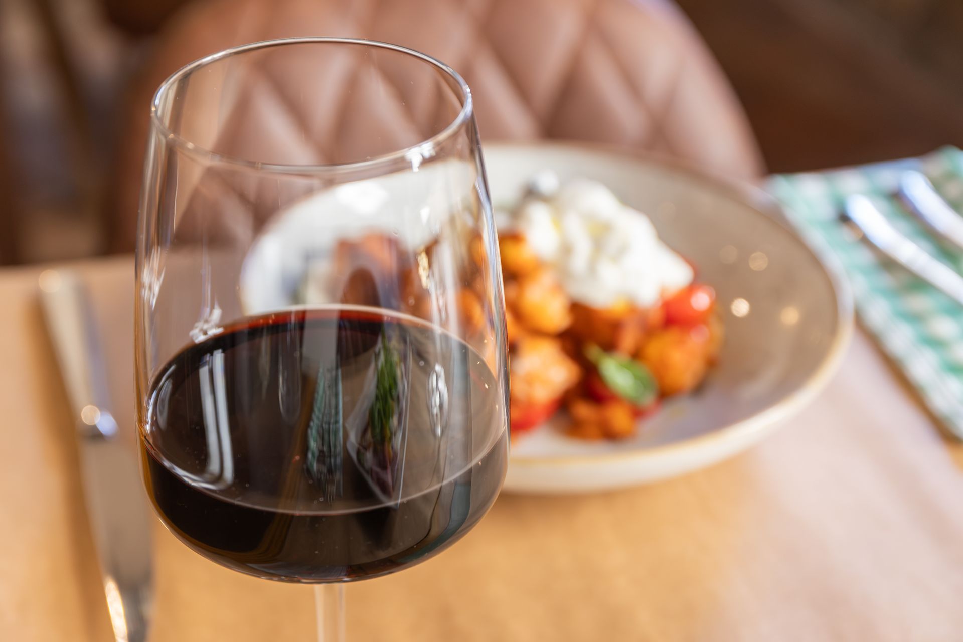 Un bicchiere di vino rosso su un tavolo di legno accanto a un piatto di cibo.