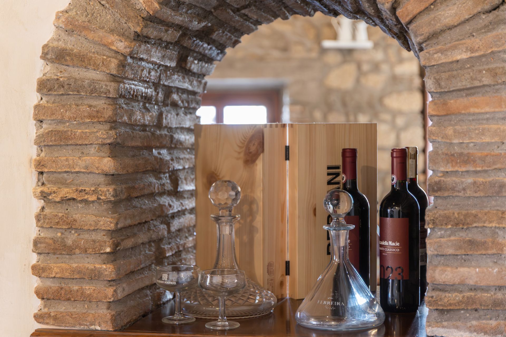 Bottiglie di vino e bicchieri su un bancone di legno sotto un arco di pietra.