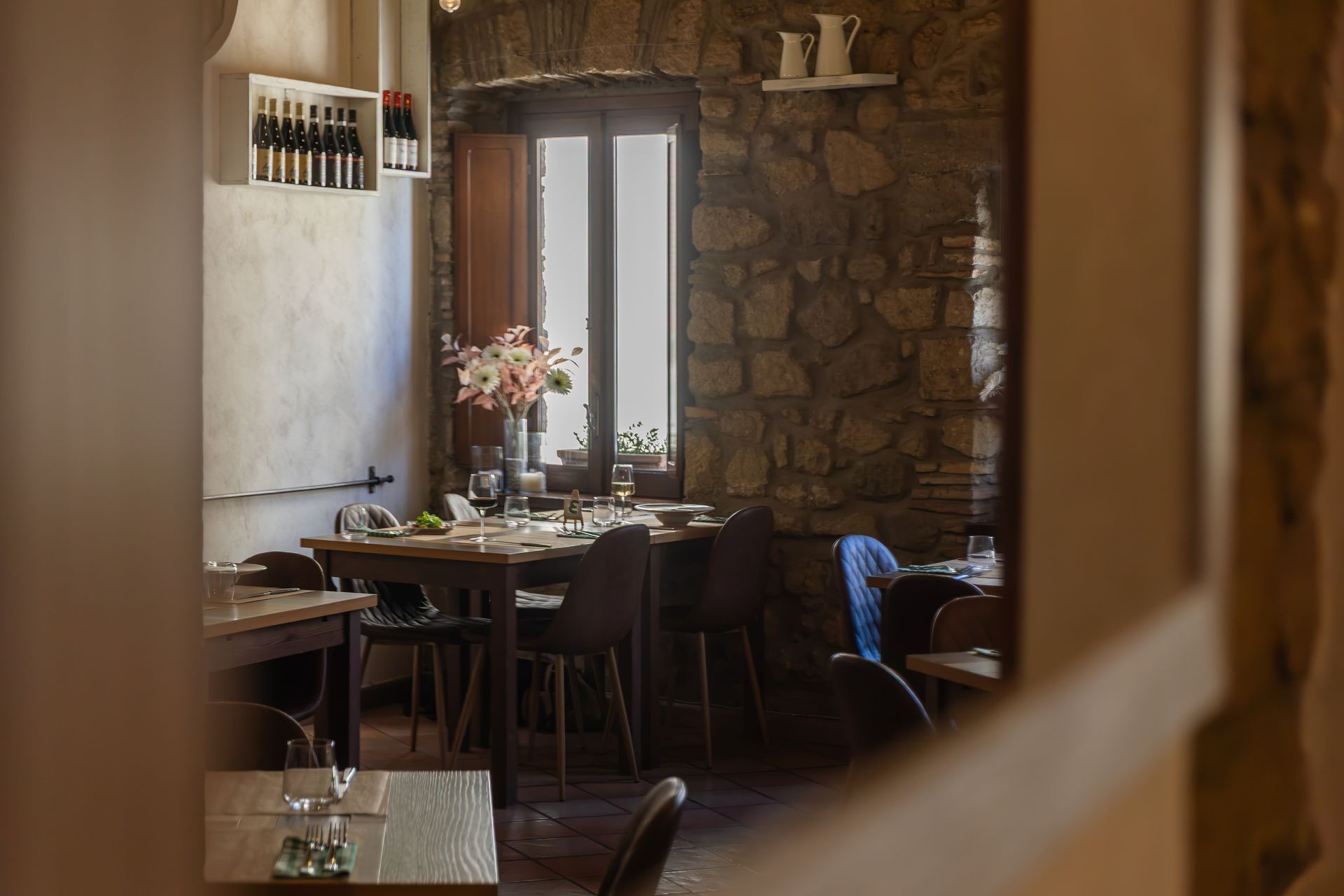 Accogliente sala da pranzo in stile rustico con parete in pietra, tavolo e sedie in legno e un vaso di fiori vicino alla finestra.