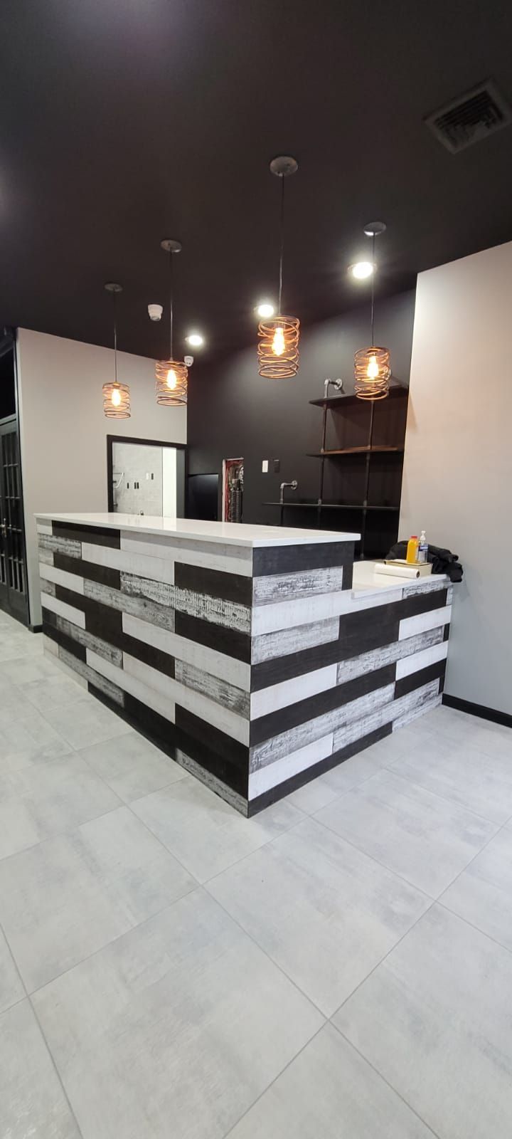 Modern reception desk in a minimalist black-and-white office lobby with hanging pendant lights.