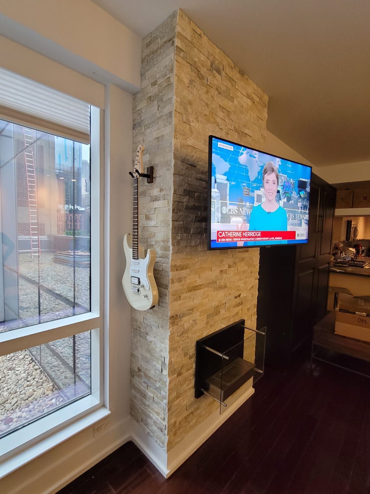 Living room with mounted TV, stone fireplace, and large window overlooking a city view