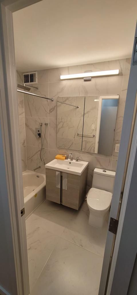 Small white bathroom with marble shower, vanity, toilet, and wall mirror in a narrow entryway