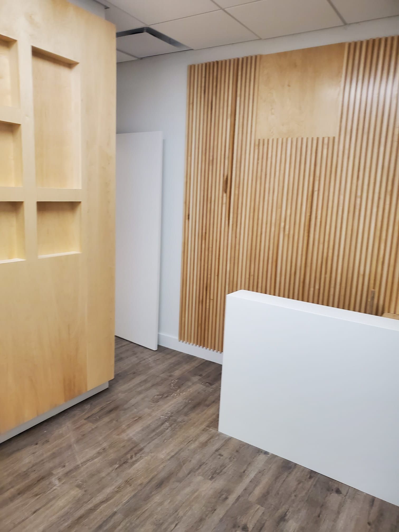 Modern office interior with wood-paneled wall, white partition, and wood flooring.
