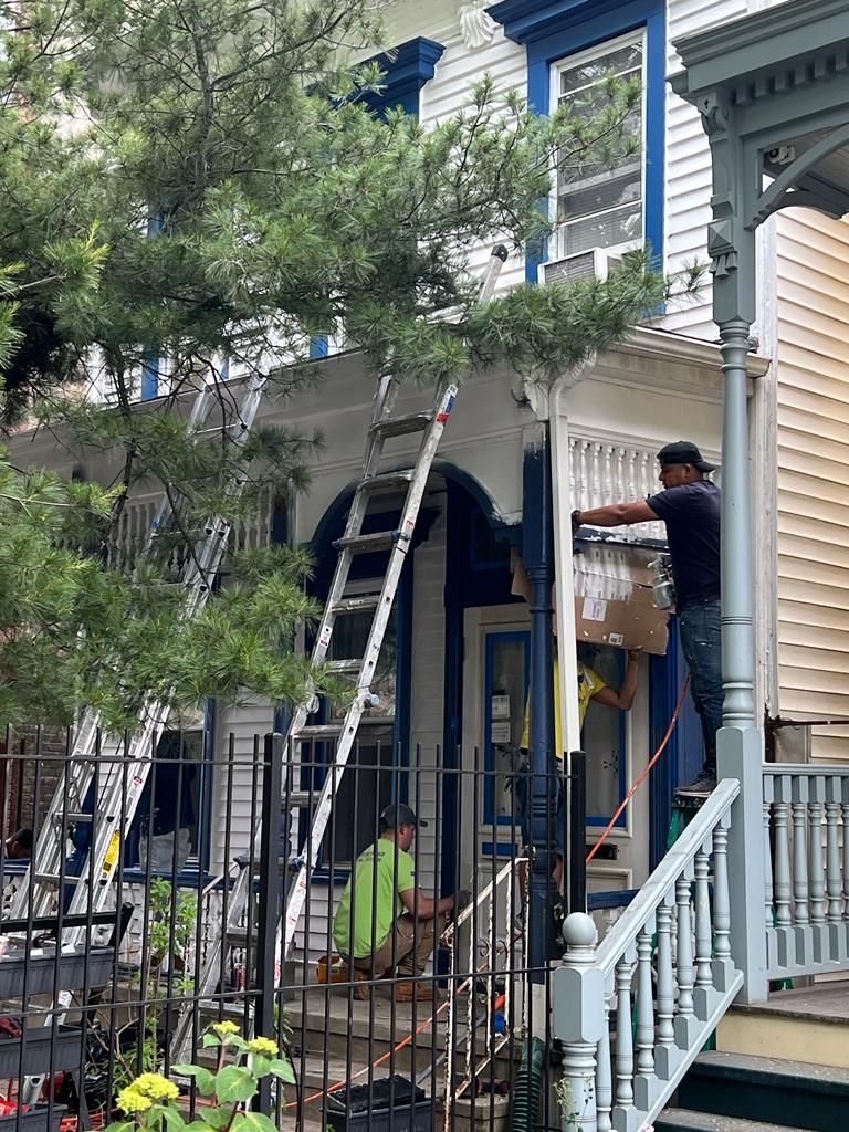Worker on a ladder painting the exterior of a blue house with white trim.