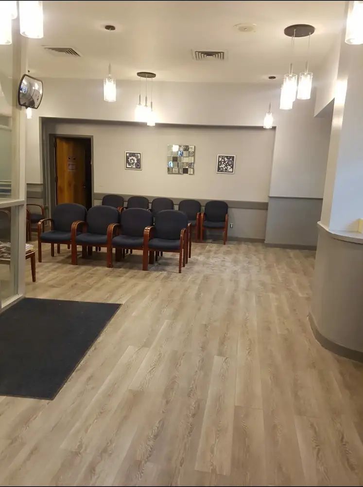 Empty waiting room with blue chairs, light wood floor, and pendant lights on the ceiling.