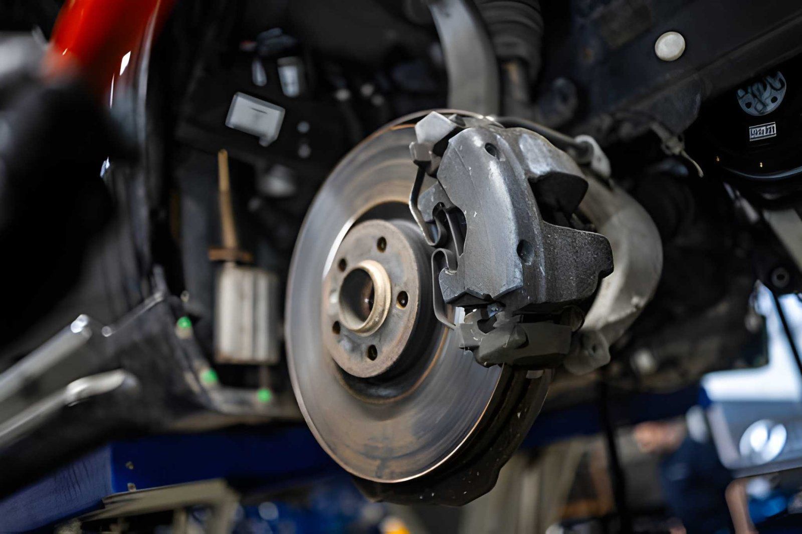 Car brake rotor and caliper in a vehicle repair shop, close-up view.
