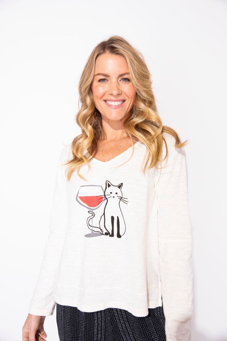 A woman wearing a white sweater with a cat and a glass of wine on it