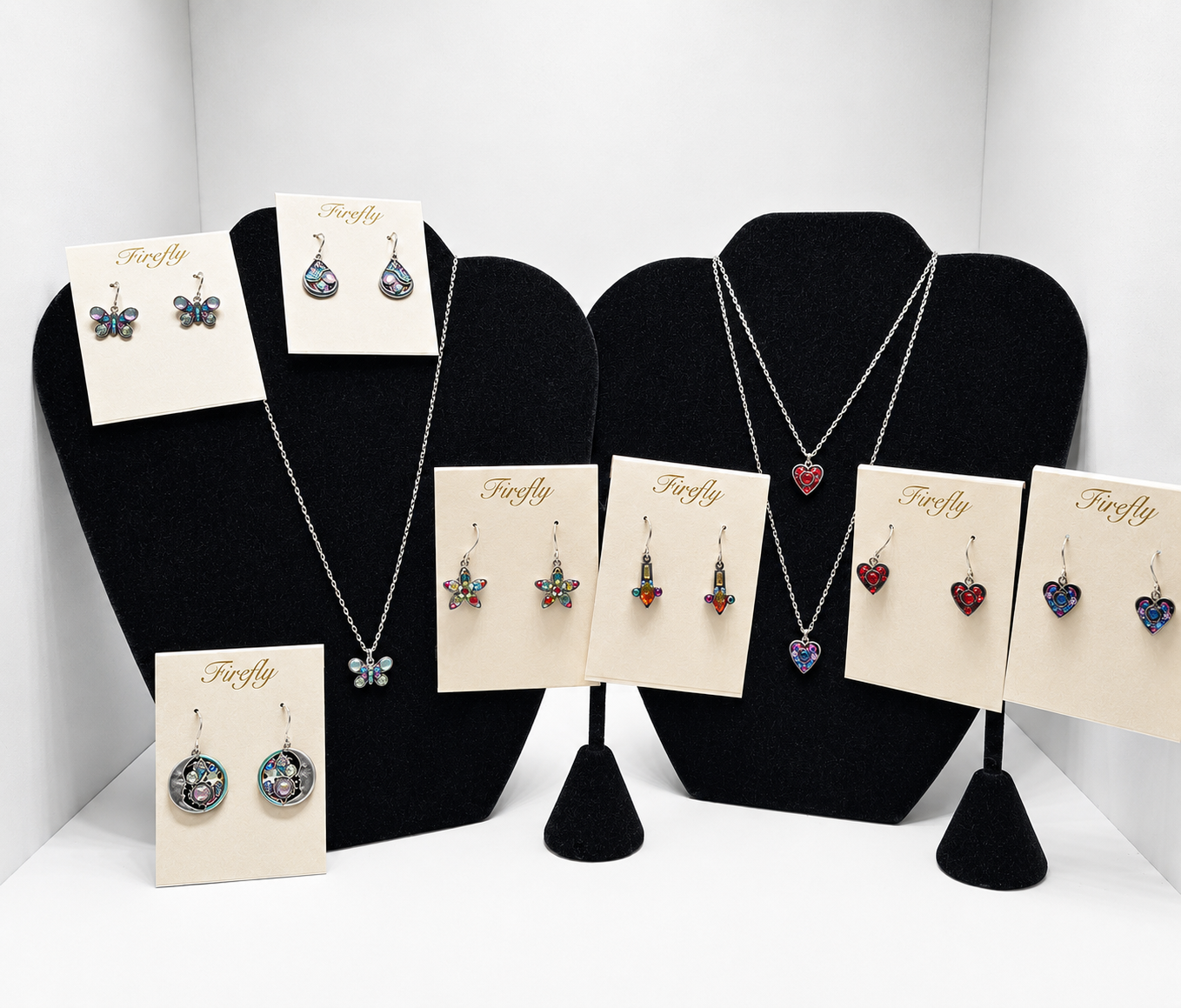 Earring and necklace display on black busts, with colorful jewelry cards arranged in a white display box