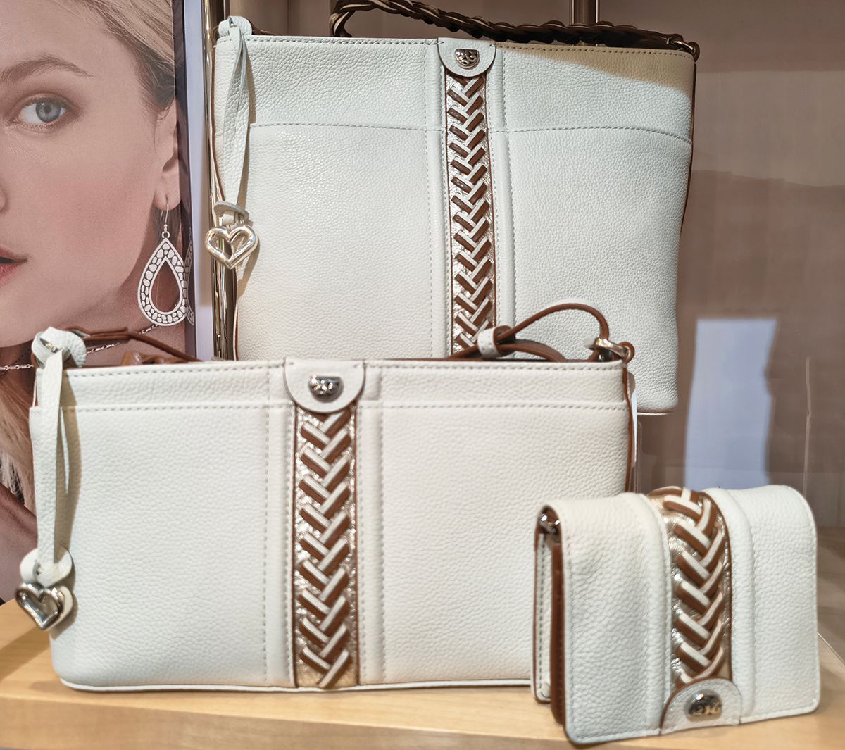 Three white handbags with gold accents displayed on a shelf, with one small matching purse in front.