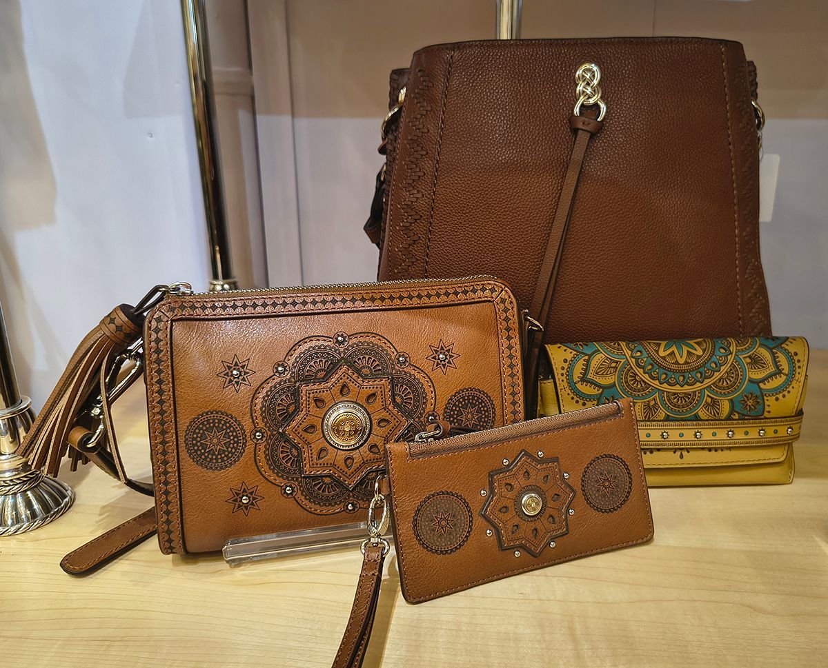 Two brown floral handbags and a matching wallet displayed on a table.