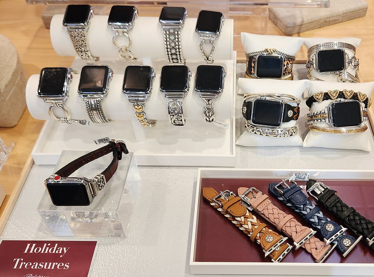 Display of multiple smartwatch bands in black, gold, silver, and patterned styles on trays and stands