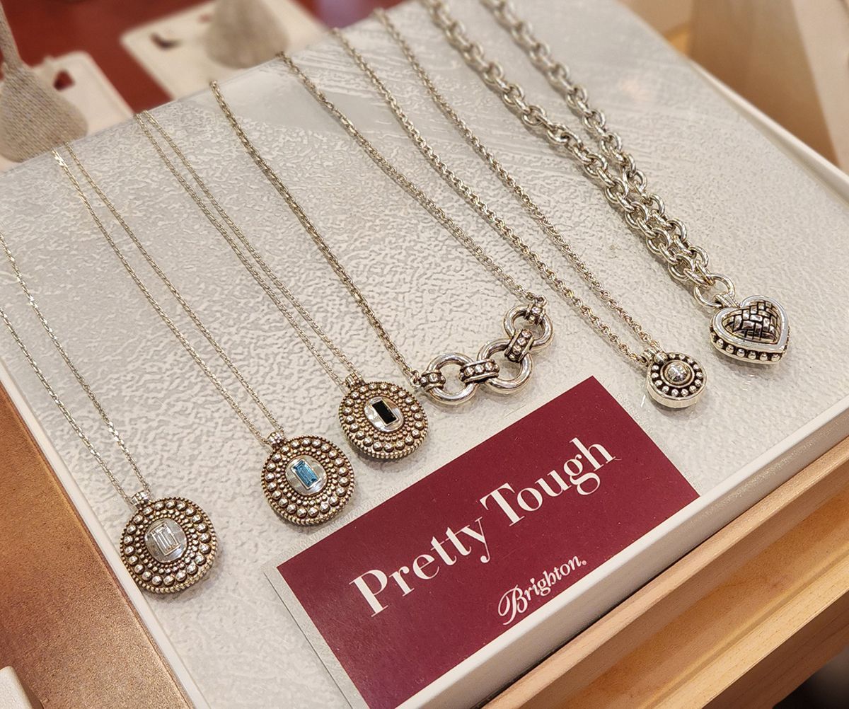 Silver and gold pendant necklaces displayed on a tray with a red “Pretty Tough” card