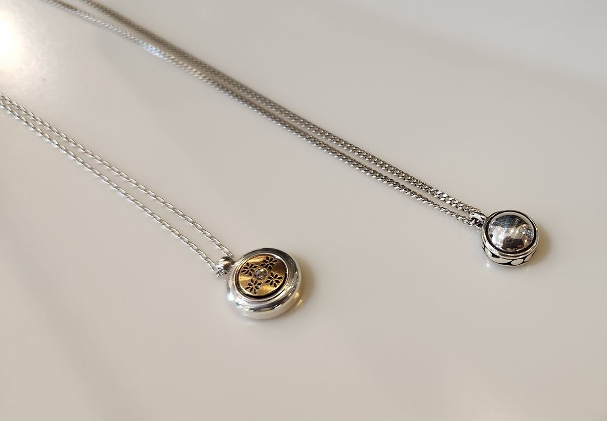 Two silver pendant necklaces with round charms, one gold-toned and one clear, on a light surface