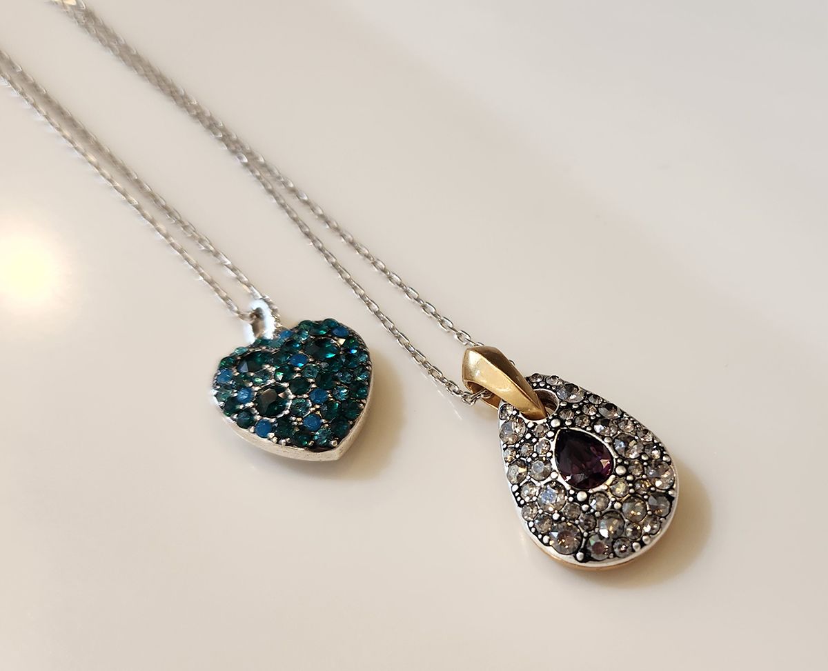 Two pendant necklaces: one blue heart and one silver teardrop with a dark center