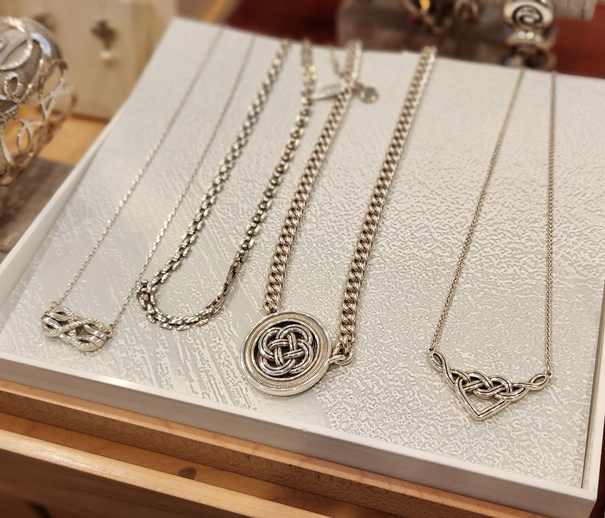 Display of gold and silver necklaces on a cream jewelry tray, including chains and pendants