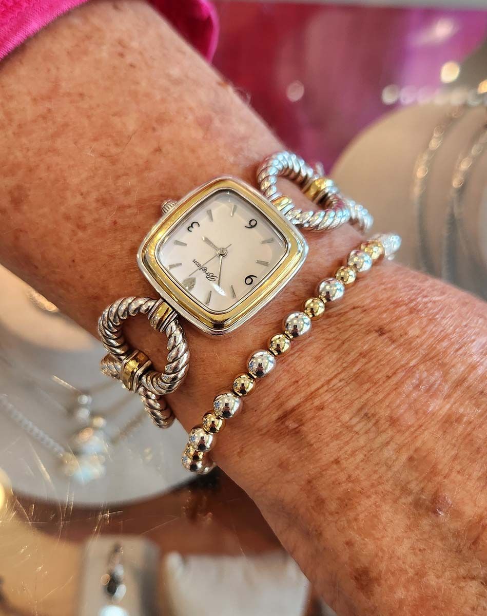 Close-up of a wrist wearing a gold watch and two bracelets on a pink background
