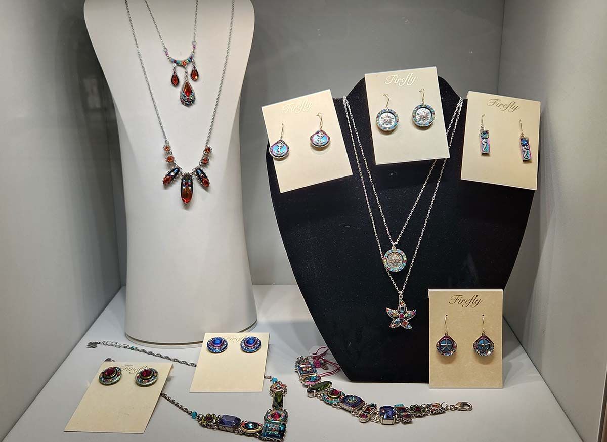 Jewelry display with necklaces, earrings, and bracelets on white and black stands in a shop window