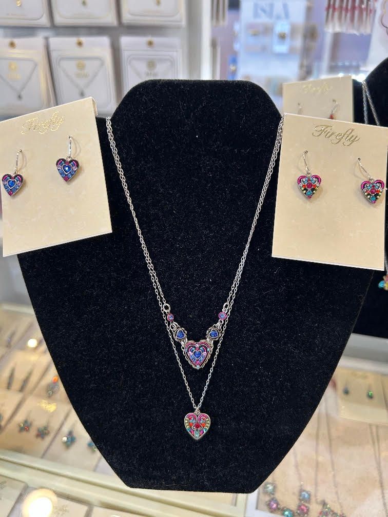 Black jewelry display bust with silver necklace and heart-shaped blue-pink pendant set, plus matching earrings on cards