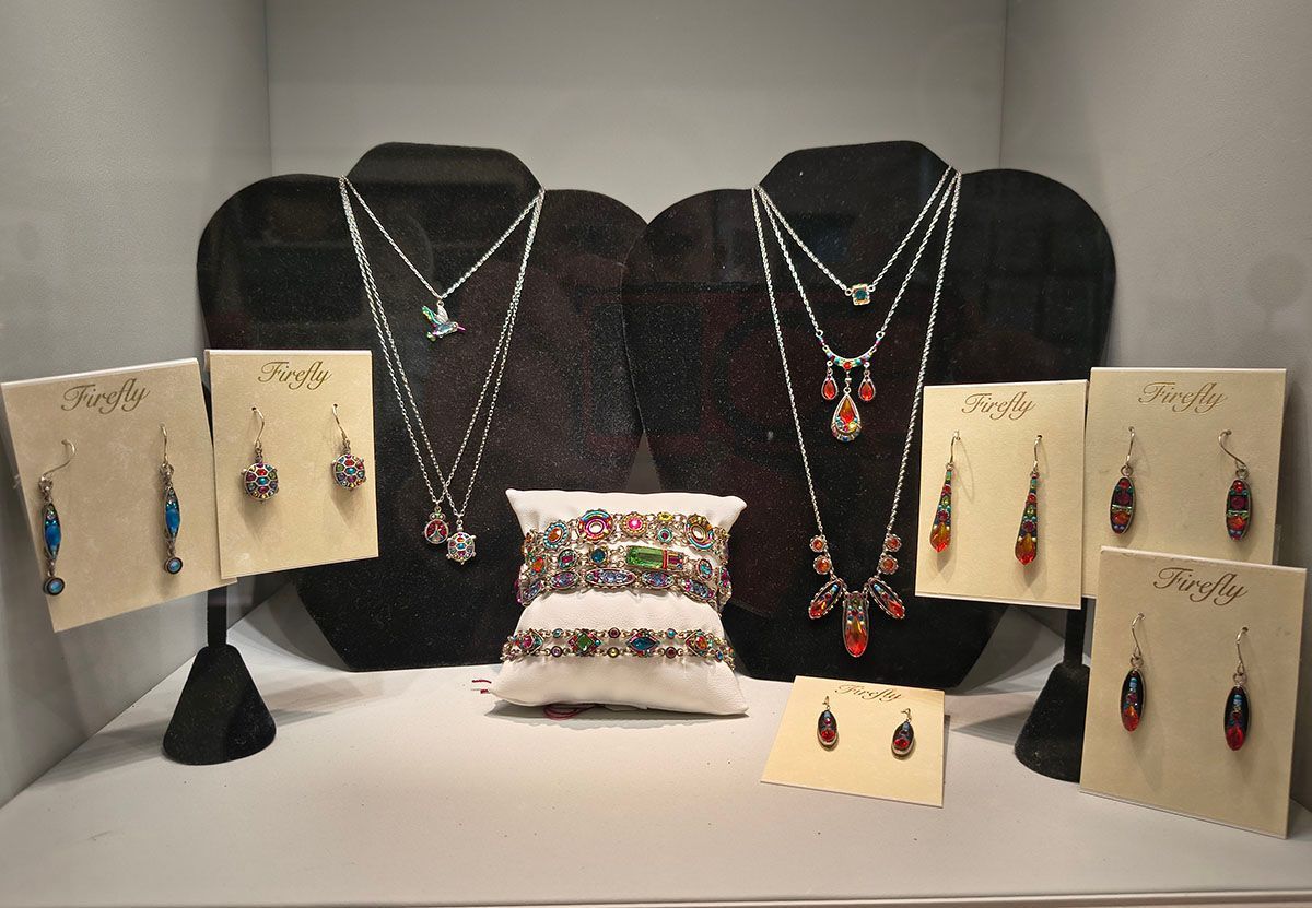 Jewelry display with necklaces, earrings, and rings arranged on black stands and cream cards with a decorative pillow center