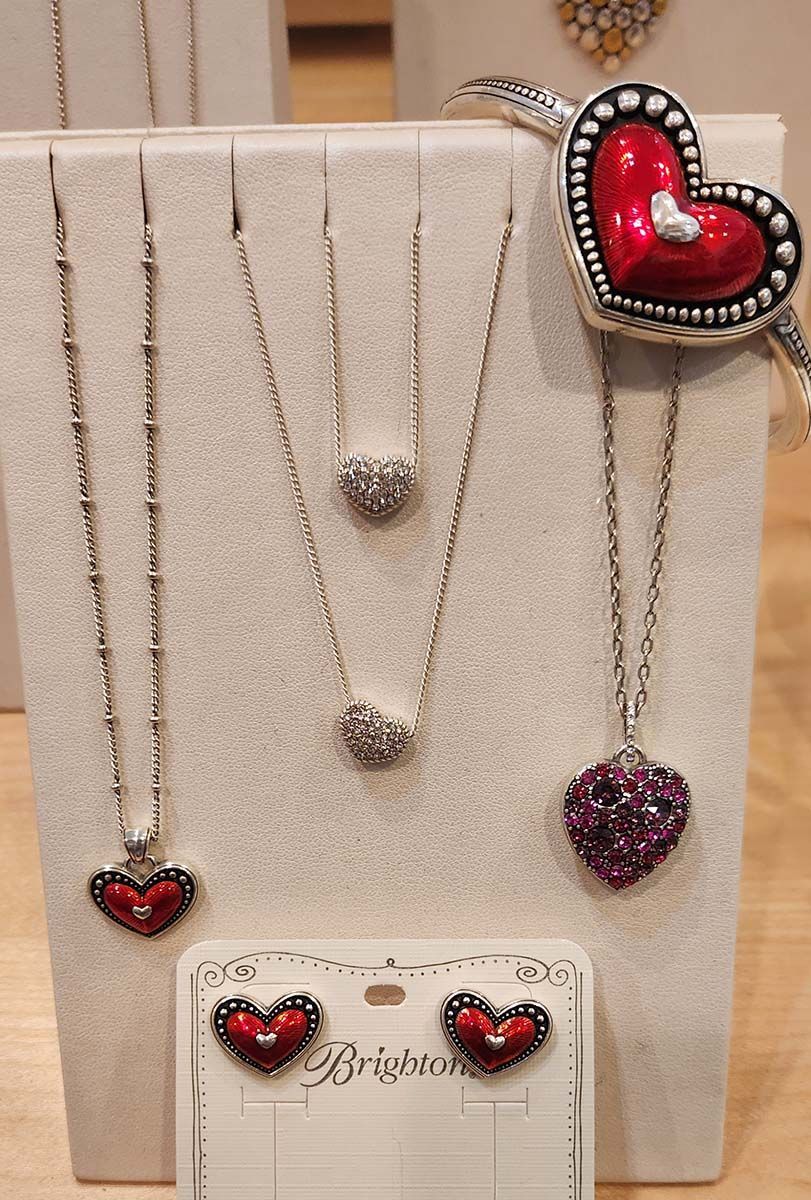 Display of heart-shaped necklaces and earrings on a beige stand with red and silver accents