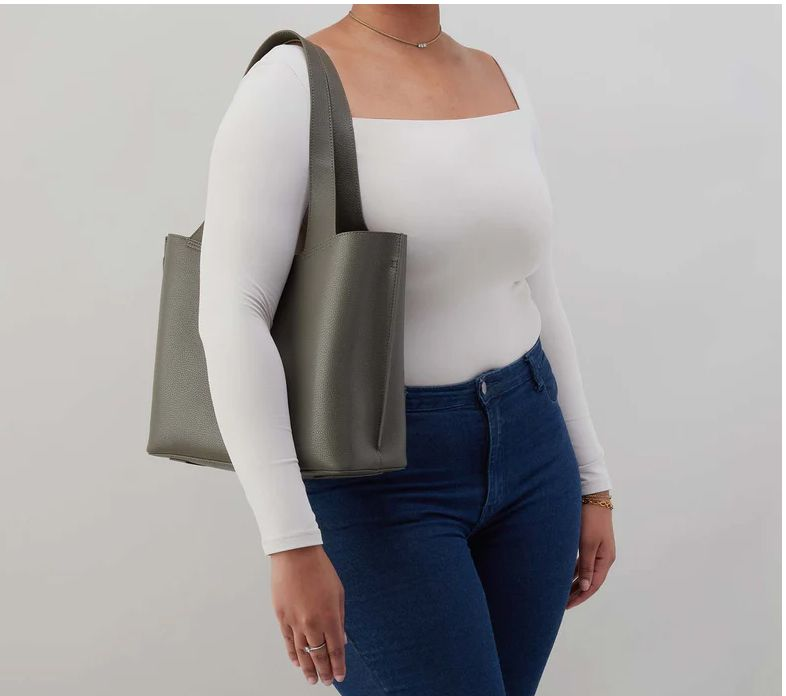 Person wearing a white top and blue jeans carrying a gray tote bag on one shoulder