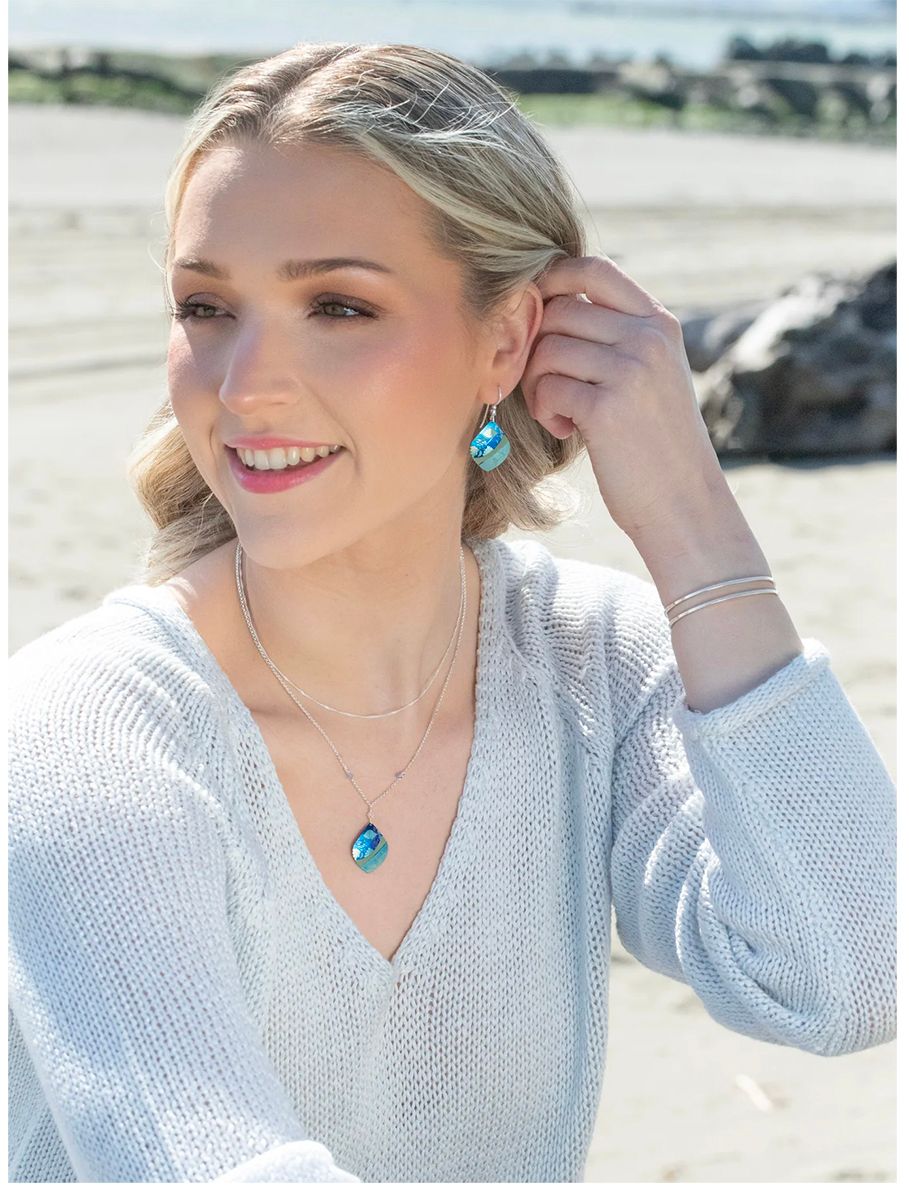 Woman in a white sweater adjusting an earring outdoors on a sunny beach