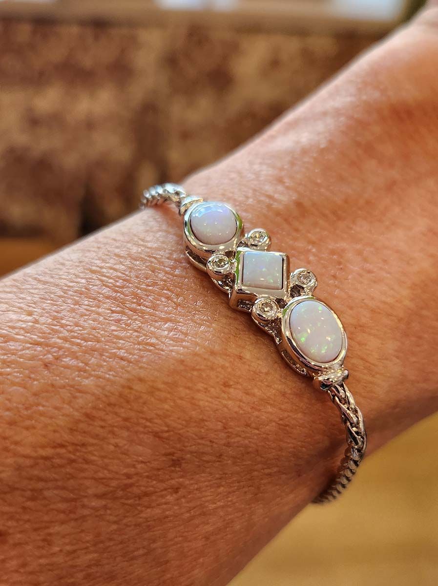 Hand wearing an opal and crystal bracelet on a wrist, close-up against a blurred background