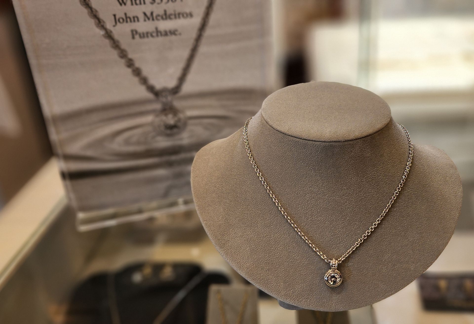 Gold necklace displayed on a beige jewelry bust with a round pendant
