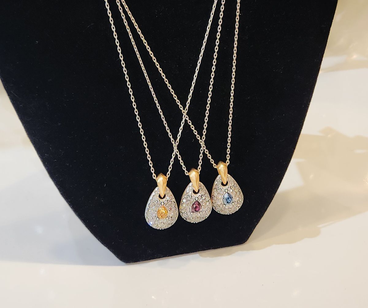 Three gold pendant necklaces with colorful stones displayed on a black velvet stand.
