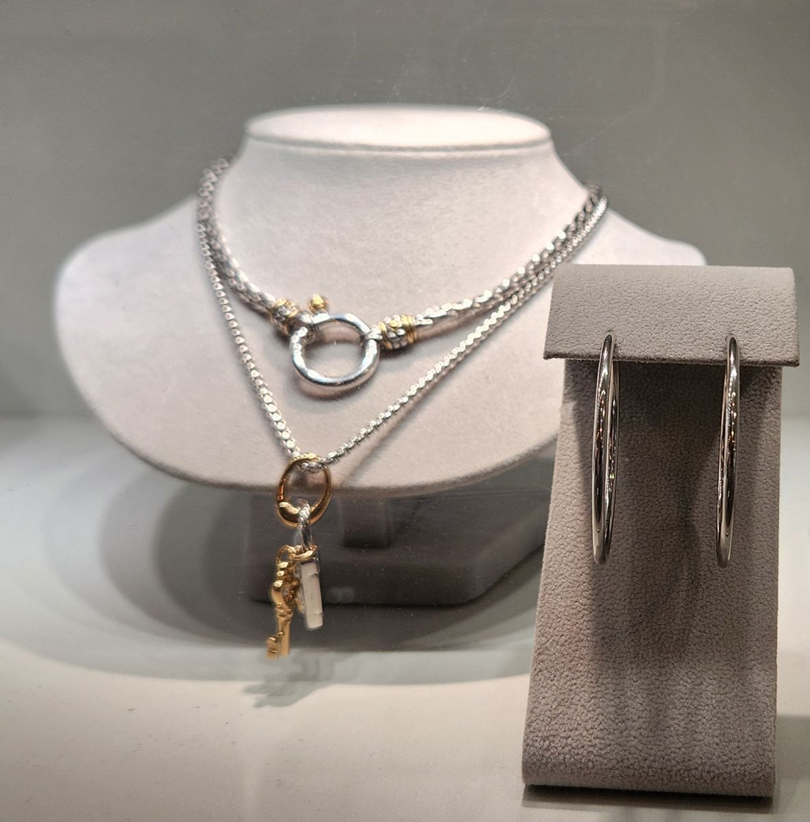Silver necklaces and hoop earrings displayed on gray jewelry bust and stand