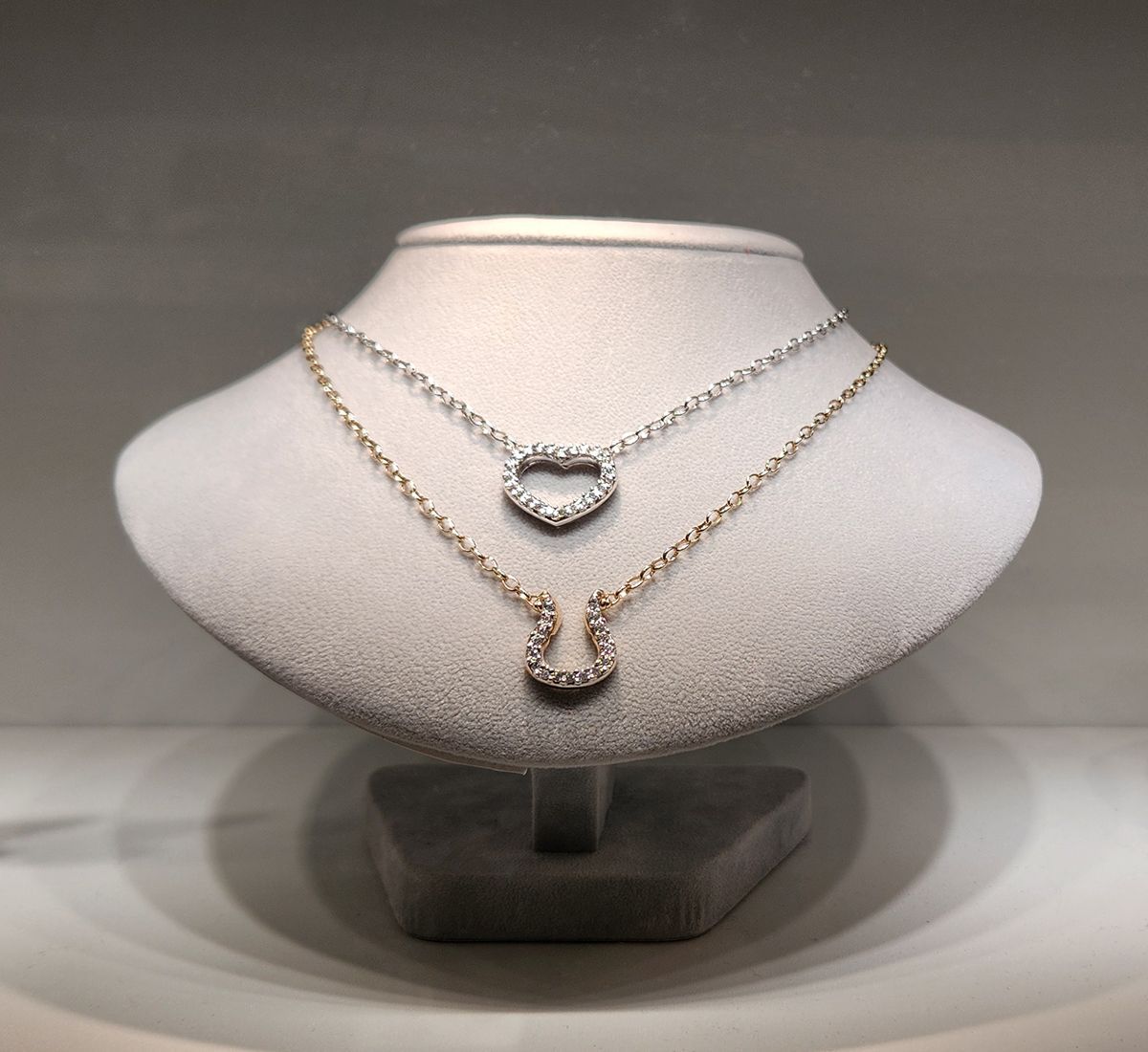 Two layered gold necklaces with a diamond pendant displayed on a white jewelry bust