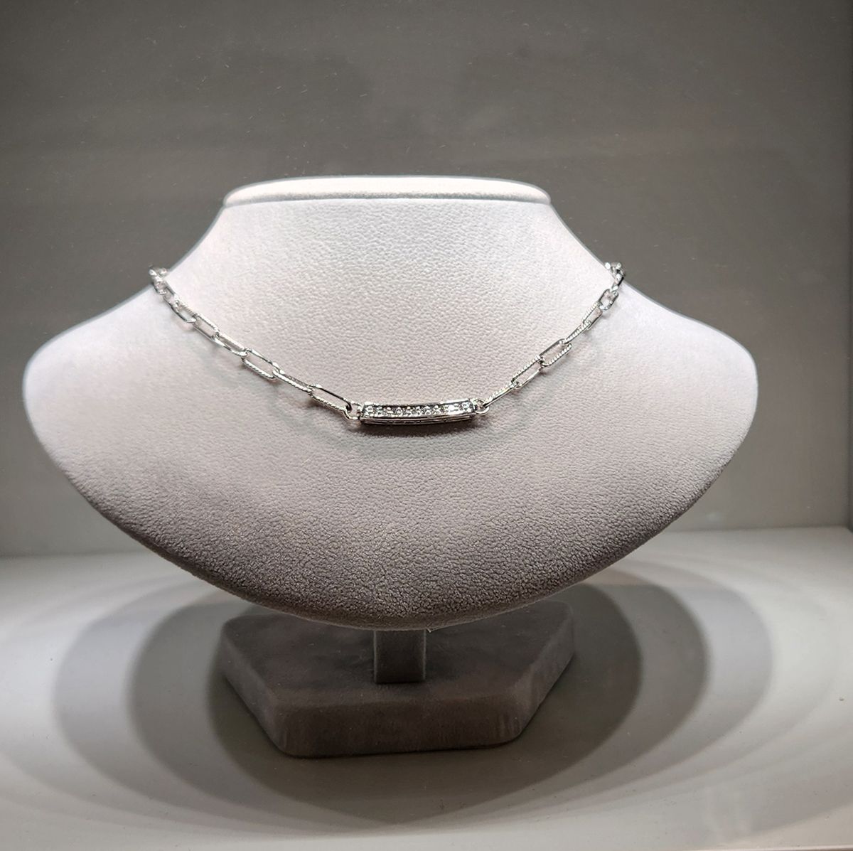 Silver necklace displayed on a gray velvet bust stand against a neutral background