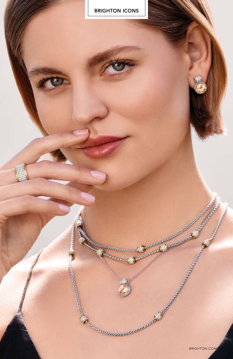 Woman modeling layered silver jewelry on a soft pink background