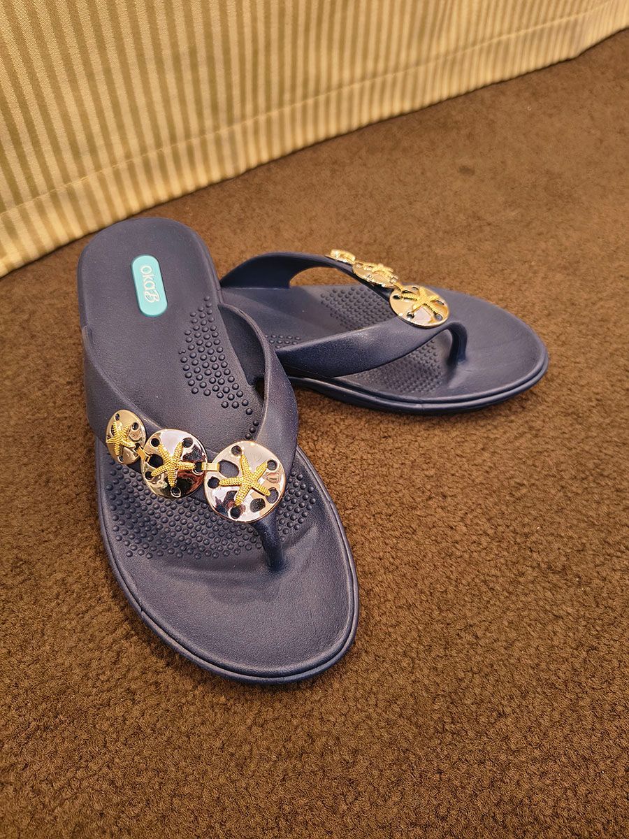 Pair of navy flip-flops with gold beaded straps on a brown carpet.